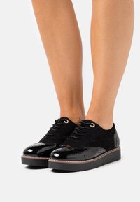 Scarpe brogue nere con un mix di pelle scamosciata e pelle verniciata, dotate di dettagli perforati, punta rotonda e suola platform.