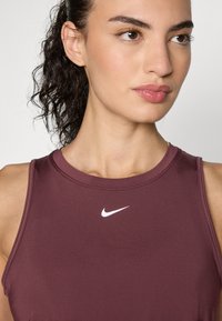 Burgundy athletic tank top made of smooth fabric features a round neckline and a small white Nike logo on the chest.