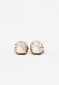 Deux chaussures slip-on métalliques dorées avec une texture tissée et des accents lisses au niveau du talon, dotées d'une semelle en caoutchouc plate.