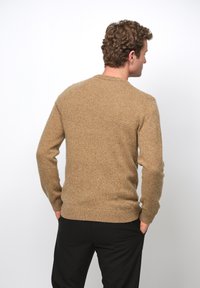 Bruine gebreide trui met een geribbelde ronde hals, lange mouwen en een gestructureerde afwerking. Gedragen over zwarte broek, met zicht op de achterkant.