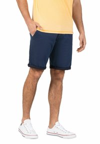 Navy blue shorts with a rolled hem, made of cotton blend fabric; paired with a light yellow t-shirt and white sneakers.
