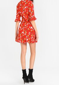 Rotes Blumenkleid mit kurzen, gerafften Ärmeln, tailliertem Schnitt und schwingendem Rock. Getragen mit schwarzen Knöchelstiefeln.
