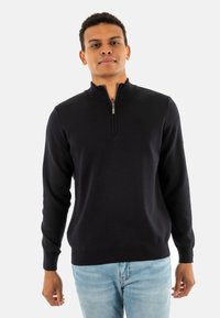 Maglione zip navy in morbido tessuto a maglia, con colletto alto e polsini a coste, abbinato a jeans azzurri chiari.