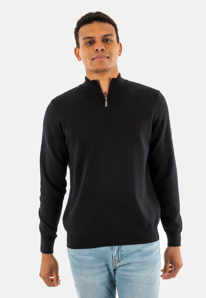 Maglione zip navy in morbido tessuto a maglia, con colletto alto e polsini a coste, abbinato a jeans azzurri chiari.