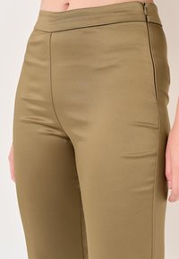 Tannengrüne, figurbetonte Hose aus einem glatten, dehnbaren Stoff. Mit hoher Taille, seitlichem Reißverschluss und dezenten Nahtdetails.