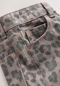 Close-up of leopard print denim fabric showing front pocket, belt loop, and copper rivet detail.