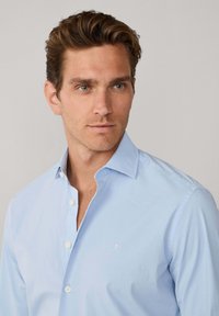 Lichtblauw katoenen overhemd met knopen. Voorzien van een klassieke kraag, een subtiel logo op de linkerborst en standaard manchetten. Gladde textuur.