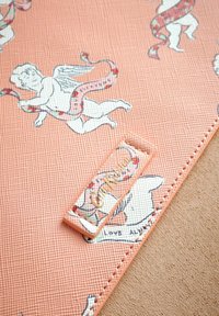Pestový textil s rímskymi anjelikmi a stuhami v broskyňovej farbe, s obdĺžnikovým štítkom, na ktorom je nápis "Cat Kid" obkreslený svetlejšou farbou.