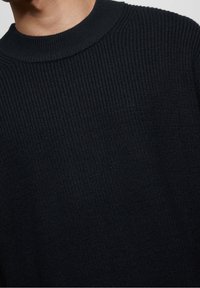 Pull en maille foncée avec une surface texturée, présentant un col ras du cou côtelé et des manches courtes.