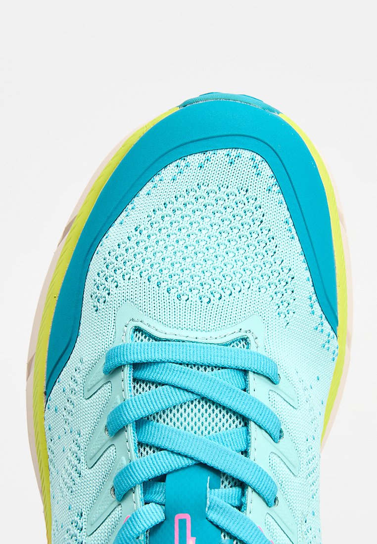 Zapatilla deportiva azul claro con parte superior de malla, suela de goma, detalles en verde azulado y logo rosa. Presenta cordones redondos y diseño reforzado en la puntera.