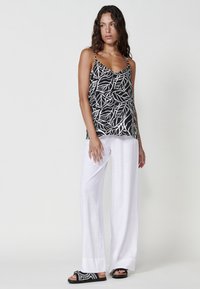 Top à bretelles fines avec un motif de feuilles noir et blanc, associé à un pantalon en lin blanc ample et des sandales noires avec des accents tissés.