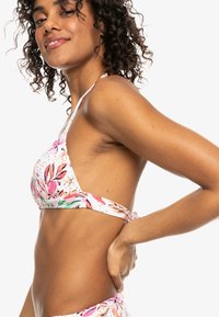 Bloemrijke bikinitop met een witte basis, voorzien van roze en groene tropische patronen, driehoekig ontwerp en verstelbare strikbanden aan de achterkant.
