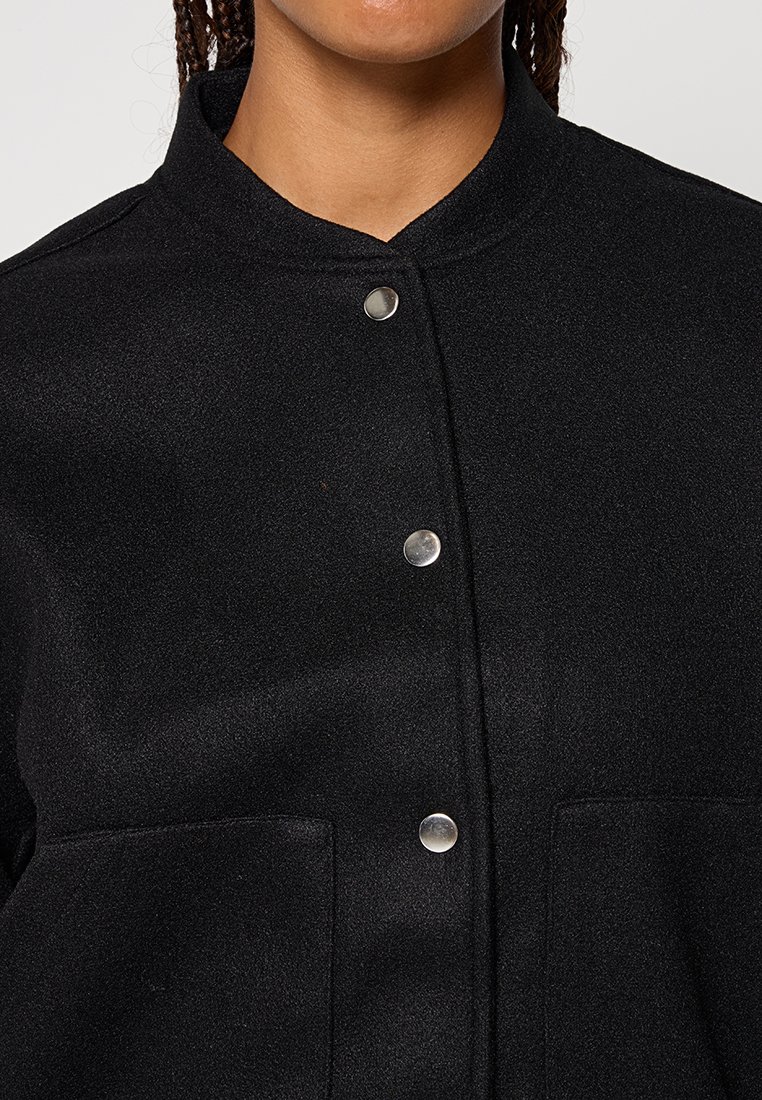 Schwarze, strukturierte Wolljacke mit Stehkragen, silbernen Druckknöpfen und zwei Vordertaschen.