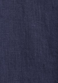 Texture de tissu tissé bleu foncé avec un motif de hachures croisées visible et de fils fins créant une surface légèrement rugueuse.