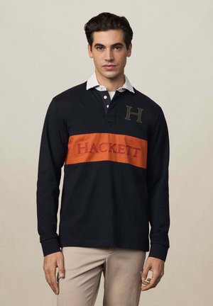 Polo a maniche lunghe della Marina con colletto bianco e fascia arancione a righe, dotato di ricamo rosso con la scritta "HACKETT" e di una "H" ricamata.