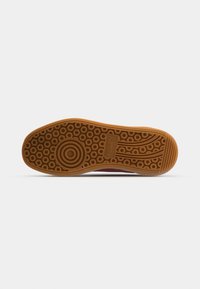 Gummisohle des Sneakers in Braun mit einem strukturierten Muster, das kreisförmige und lineare Designs aufweist. Verstärkter Zehenbereich auf einem weißen Obermaterial.