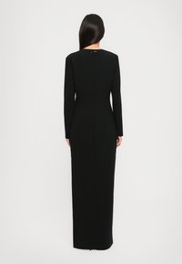 Lang zwarte jurk met lange mouwen, getailleerde pasvorm, zachte textuur, hoge halslijn en ritsdetail op de rug, minimalistisch ontwerp.