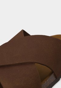 Καφέ σανδάλι από καστόρι με φαρδιές διασταυρούμενες λουράκια και φελλό σόλα, κοντινή άποψη που εστιάζει στο πάνω εμπρόσθιο σχέδιο.