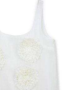 Weißes Tanktop mit drei Textilblumen in unterschiedlichen Größen, vor einem glatten und transparenten Hintergrundmaterial.