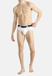 Weiße Unterwäsche mit einem schwarzen elastischen Bund, der drei Streifen aufweist. Der Stoff wirkt glatt, enganliegend und leicht.
