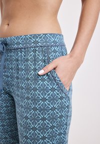 Blauwe joggers met een intricaat geometrisch patroon in verschillende tinten blauw. Voorzien van een trekkoord in de taille en zijzakken.