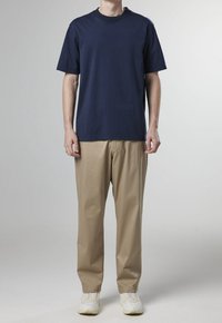 Námořnický bavlněný tričko s krátkým rukávem, spárované s béžovými volnými kalhotami a bílými teniskami, s jednoduchým designem a minimálními akcenty.