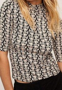 Top de manga corta con cuello alto, que presenta un patrón geométrico en negro y crema. Está hecho de una tela suave con una forma ligeramente ajustada.