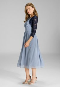 Jasnoniebieska sukienka z dopasowaną górą, koronkowymi rękawami o długości trzech kwart oraz zwiewną spódnicą. Połączona ze srebrnymi sandałami na obcasie.