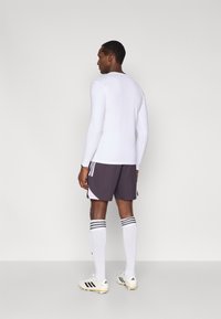 Hosszú ujjú fehér sportpóló, sötétszürke rövidnadrág fehér és rózsaszín részletekkel, fehér zokni fekete csíkokkal, valamint fehér stoplis cipő fekete csíkokkal.