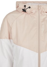 Veste à capuche beige et blanche avec fermeture éclair à l'avant et cordon noir réglable sur la capuche.