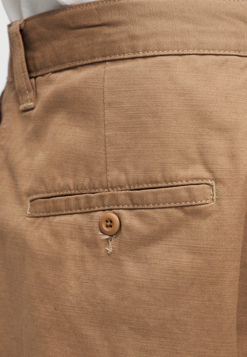 Tan trousers made of textured fabric feature a back pocket with a sewn button closure and a straight cut design.