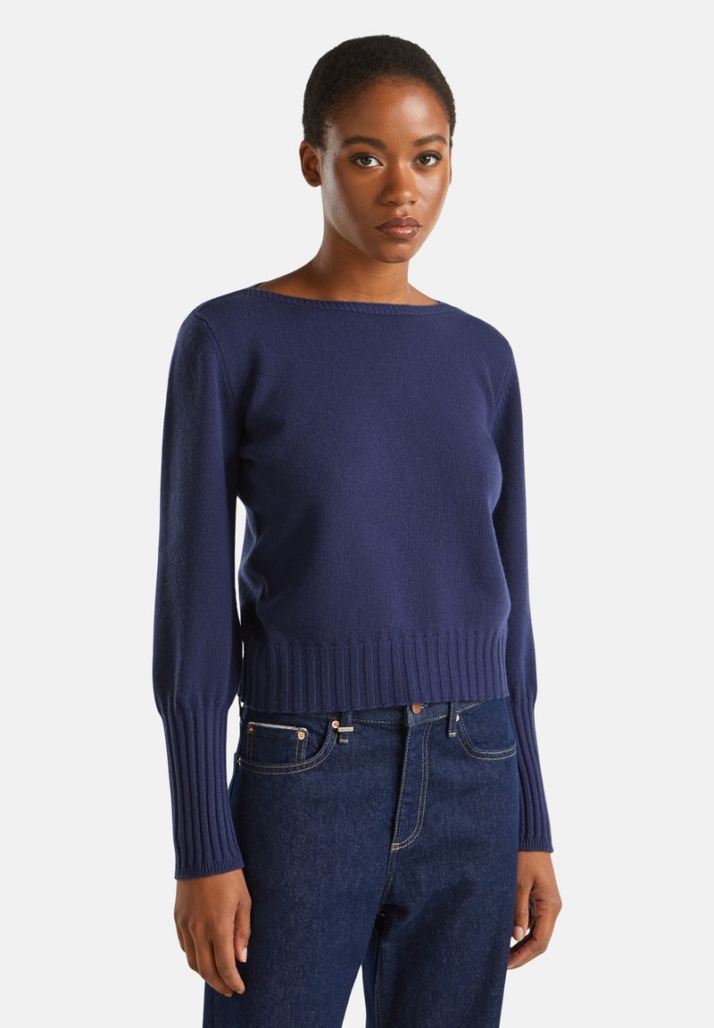 Marineblau gestrickter Pullover mit geripptem Saum und Bündchen, ausgestattet mit einem weiten Ausschnitt und einer taillierten Silhouette, kombiniert mit dunkelblauen Jeans.