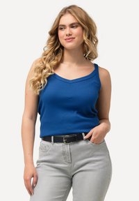 Top in maglia blu a coste con scollatura a V, caratterizzato da spalline sottili, abbinato a jeans grigi chiari a vita alta e una cintura nera.