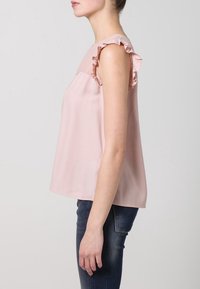 Svetle růžová bezrukávová blůza s volány na ramenou, vyrobená z hladké tkaniny, s uvolněným střihem a kulatým výstřihem.