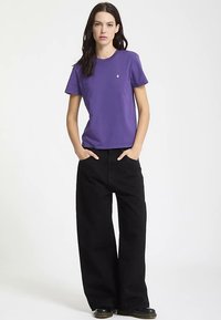 Paarse katoenen T-shirt met korte mouwen en een ronde hals, gecombineerd met loszittende zwarte broek. Zwarte schoenen maken de outfit compleet.