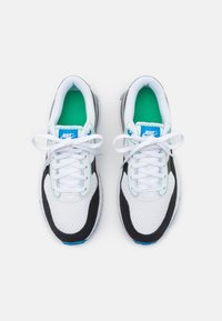 Scarpe da ginnastica bianche in rete con accenti neri, soletta turchese e lacci bianchi. Presentano il logo Nike sulla linguetta e sovrapposizioni testurizzate.