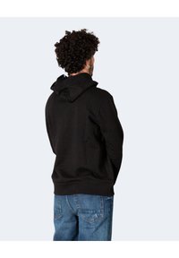 Schwarzer Hoodie mit Kängurutasche, strukturiertem Material und Kapuze mit Zugband. Kombiniert mit lässigen blauen Jeans, von hinten betrachtet.