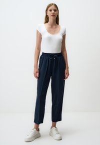Marineblauwe, loszittende broek met een elastische tailleband en trekkoord. Gecombineerd met een aansluitend wit shirt en witte sneakers.