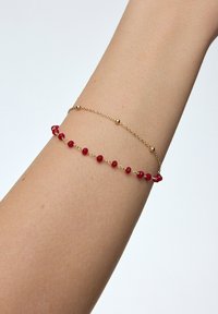 Złota bransoletka z koralikami w kolorze czerwonym, o delikatnym wzorze. Koraliki są równomiernie rozmieszczone wzdłuż łańcuszka, co nadaje jej lekkiego wyglądu.