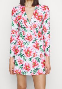 Robe-blazer à motifs floraux avec une base blanche ornée de motifs floraux roses et verts, décolleté en V profond, manches longues et coupe ajustée.