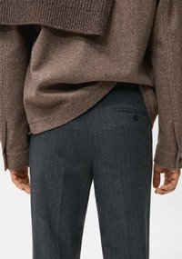 Brązowy sweter z mieszanki wełny z prążkowanymi mankietami, zestawiony z ciemnoszarymi, prążkowanymi spodniami na miarę, z tylną kieszenią i detalem guzikowym.