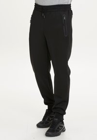 Svarta sweatpants i mjukt och elastiskt material med resårmidja. Har sidofickor med dragkedja och avsmalnade muddar.