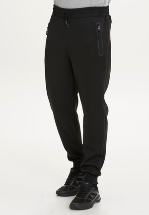 Zwarte sweatpants gemaakt van zacht, rekbaar materiaal met een elastische tailleband. Bevat zijzakken met rits en taps toelopende boorden.
