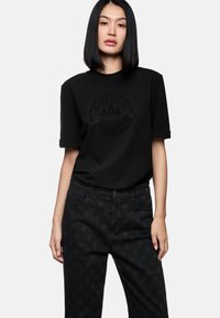Black t-shirt with a textured logo across the chest, paired with black patterned trousers featuring a star-like design.