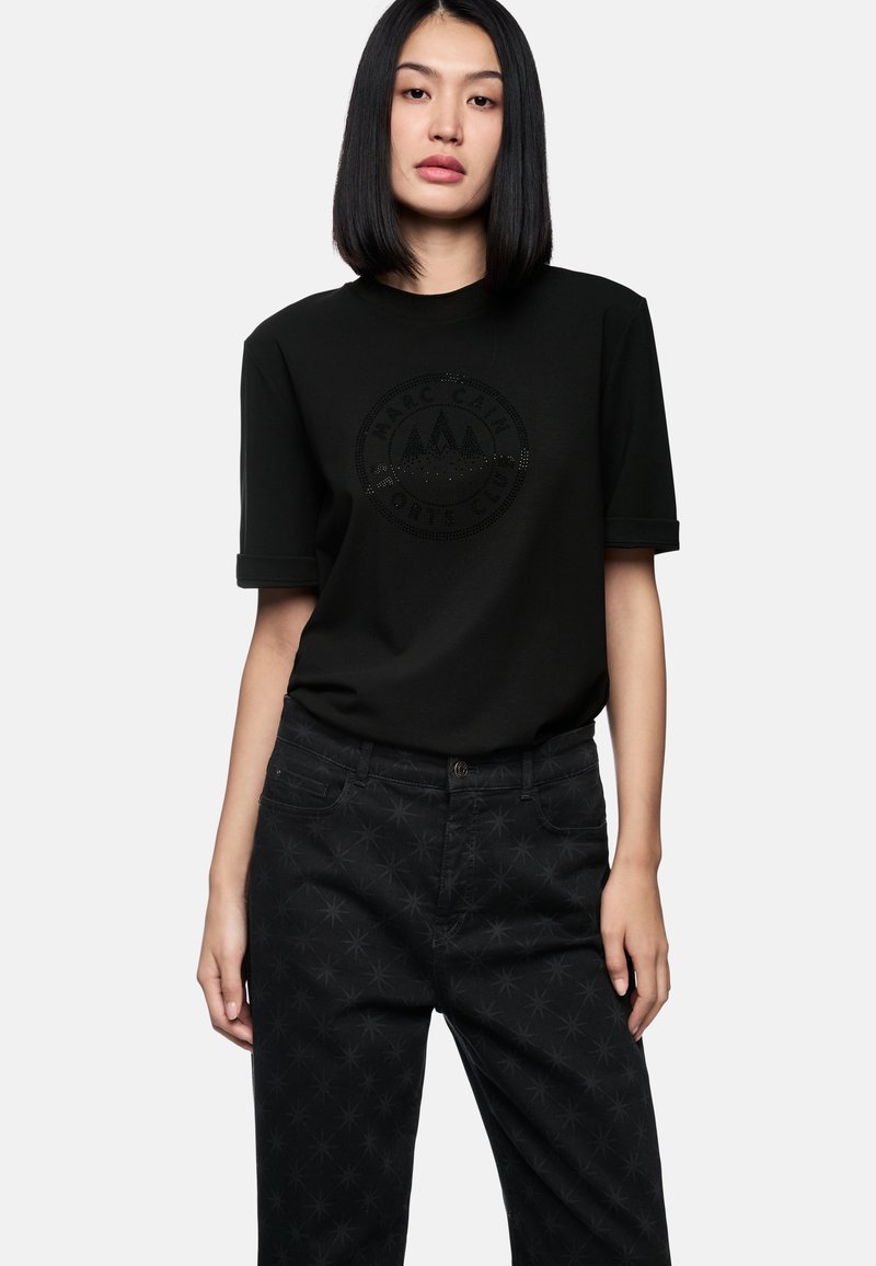 Black t-shirt with a textured logo across the chest, paired with black patterned trousers featuring a star-like design.
