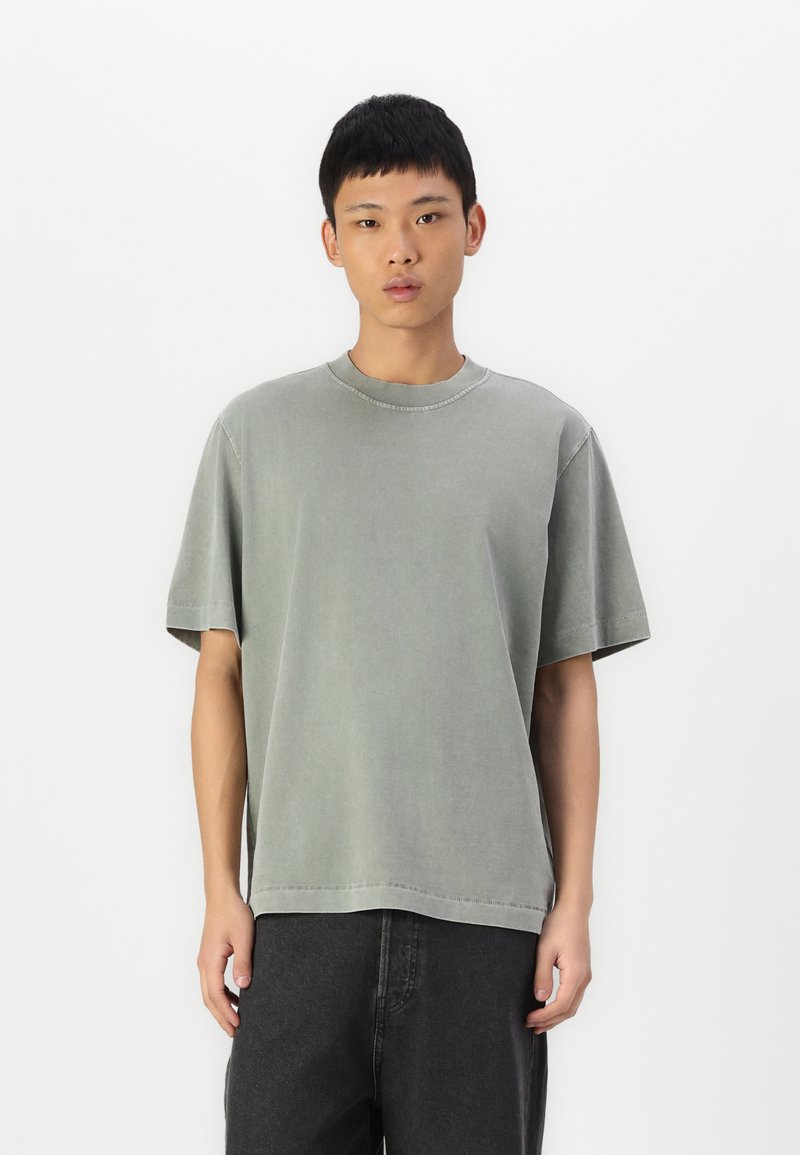 T-shirt cinza de algodão com mangas curtas, gola redonda e um corte relaxado. Apresenta costuras discretas e uma textura suave e macia.