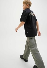 Svart bomull t-shirt med korta ärmar och logotekst på ryggen, kombinerad med löst sittande gröna cargobyxor och svarta skor.