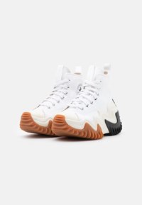 Vita hög-top sneakers med en texturerad ovandel, som har en distinkt vågig sula i orange och svart, samt snören med silverfärgade öglor.