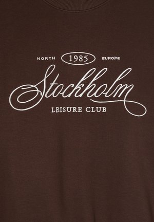 Felpa marrone con collo a girocollo e stampa bianca: "North 1985 Europe Stockholm Leisure Club." Tessuto liscio, design casual.