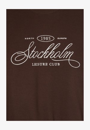 Felpa marrone con collo a girocollo e stampa bianca: "North 1985 Europe Stockholm Leisure Club." Tessuto liscio, design casual.